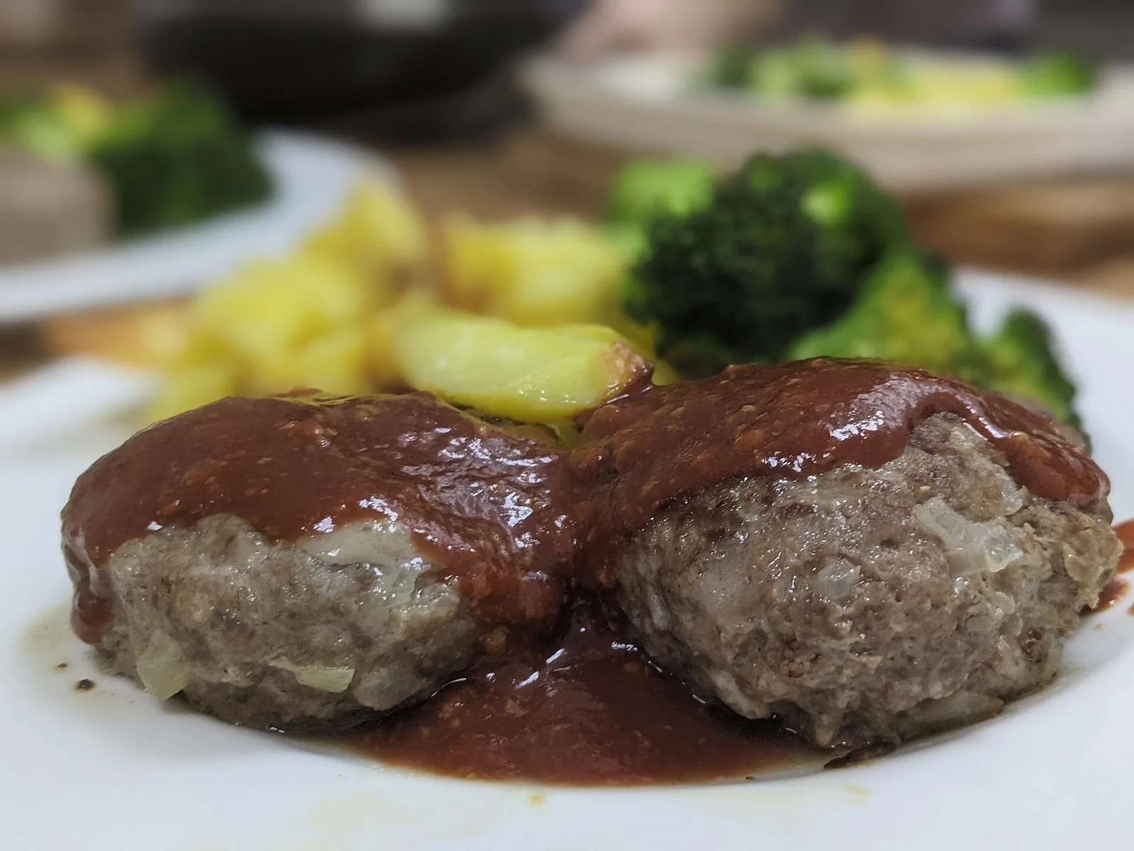 Two hamburg steaks under glossy dark demi-glace sauce on a white plate with boiled potato and broccoli.