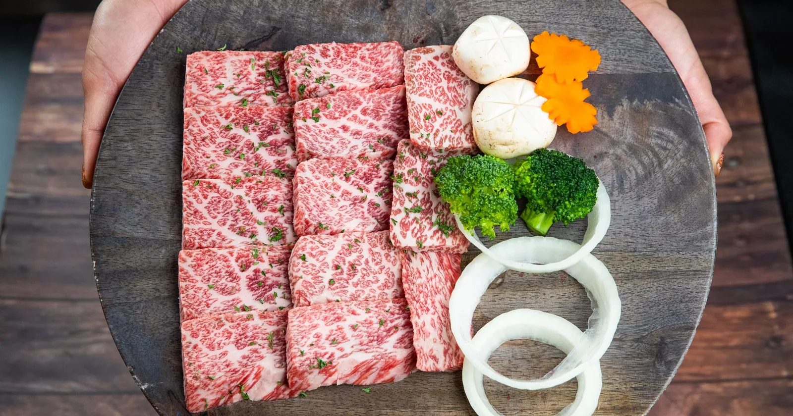 Marbled raw beef slices and vegetables on a wooden board