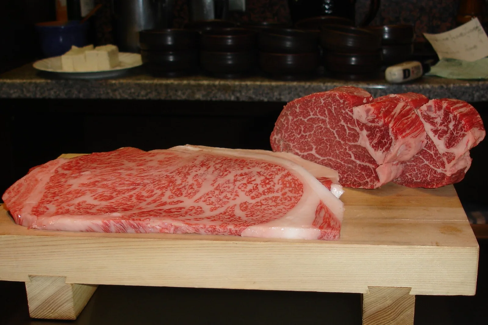 Two marbled Kobe beef cuts on a wooden stand