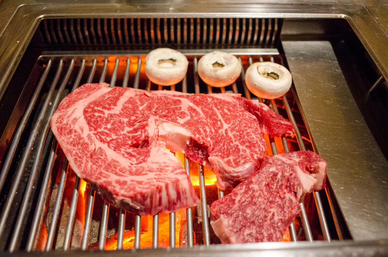 Marbled beef steaks and mushrooms on a charcoal grill