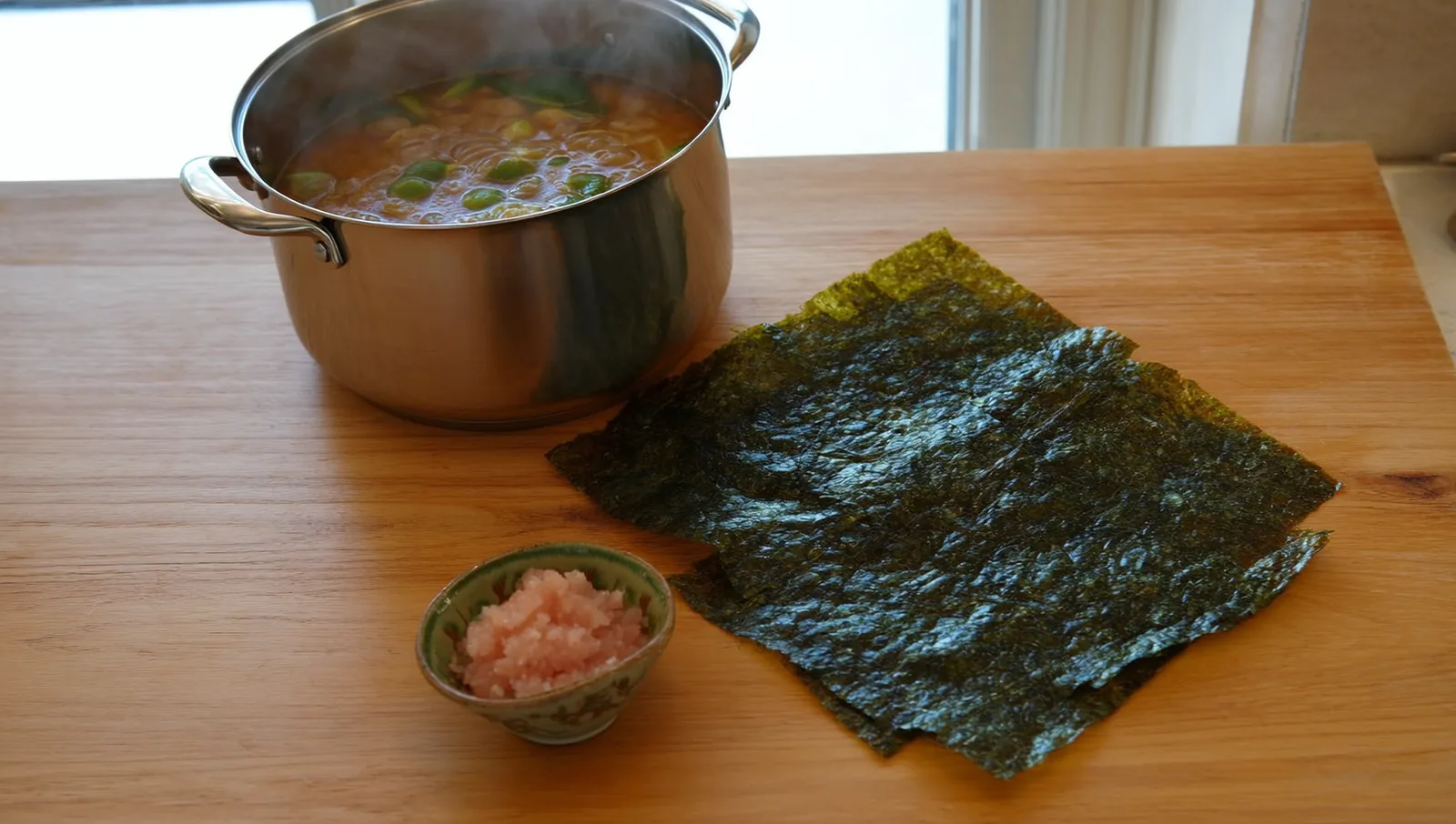 A sheet of dried kombu kelp and a bowl of pale bonito flakes beside a simmering pot, the building blocks of Japanese dashi.