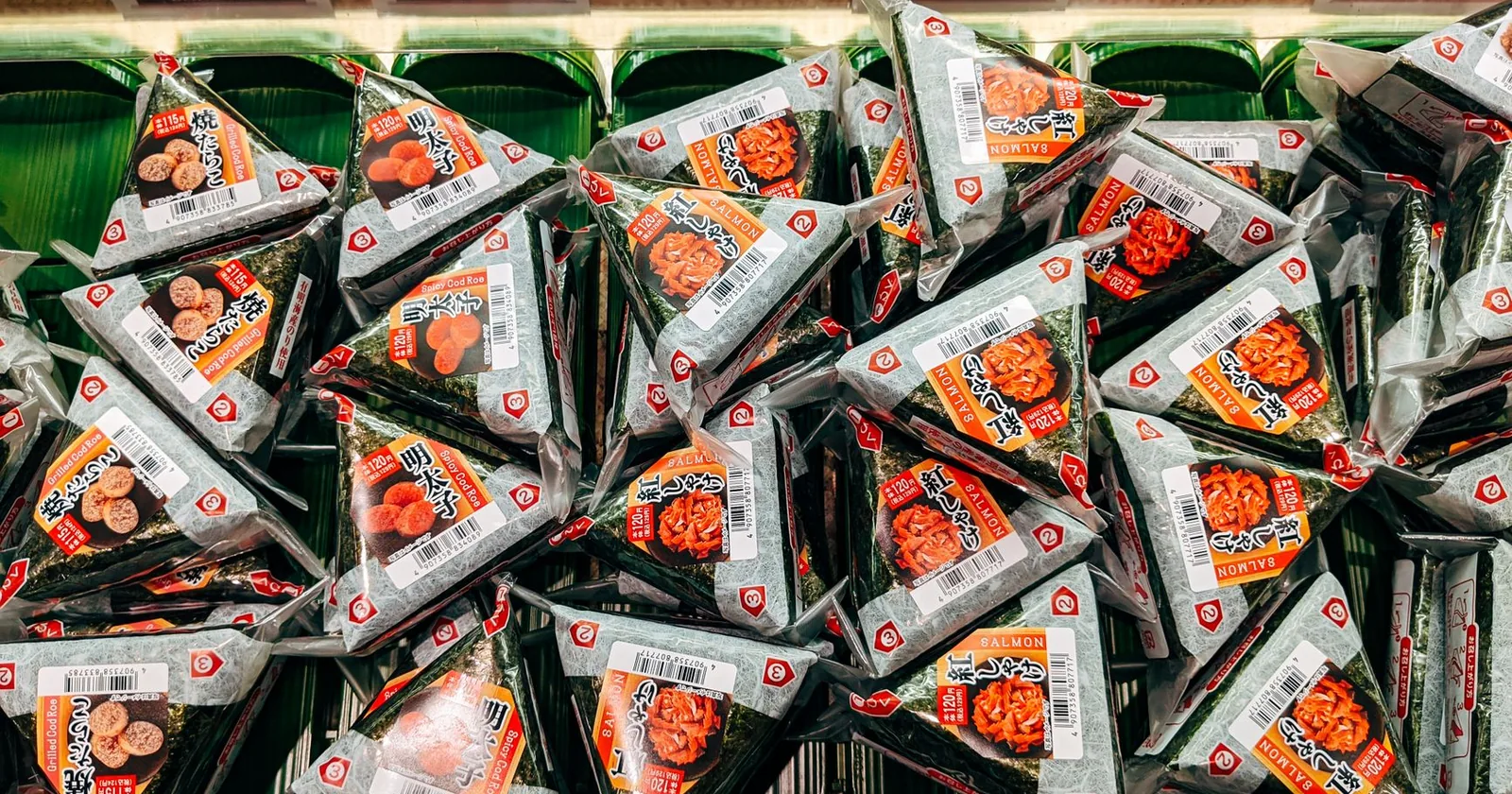 A convenience store shelf stacked with triangular packaged onigiri rice balls in their film wrappers.