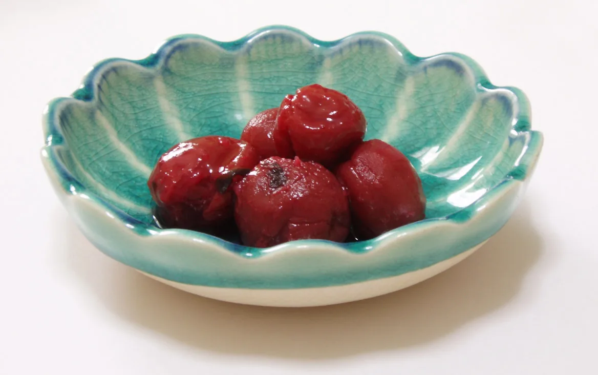 Several dark red umeboshi pickled plums in a small green ceramic dish.