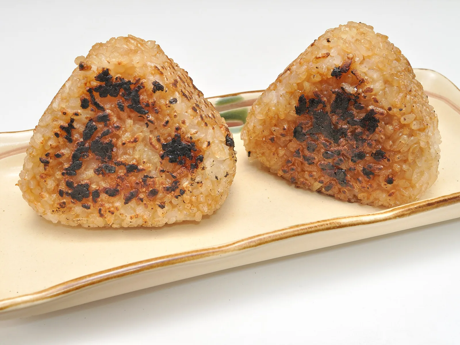 Two triangular yaki onigiri with browned and charred grilled surfaces resting on a pale ceramic plate.