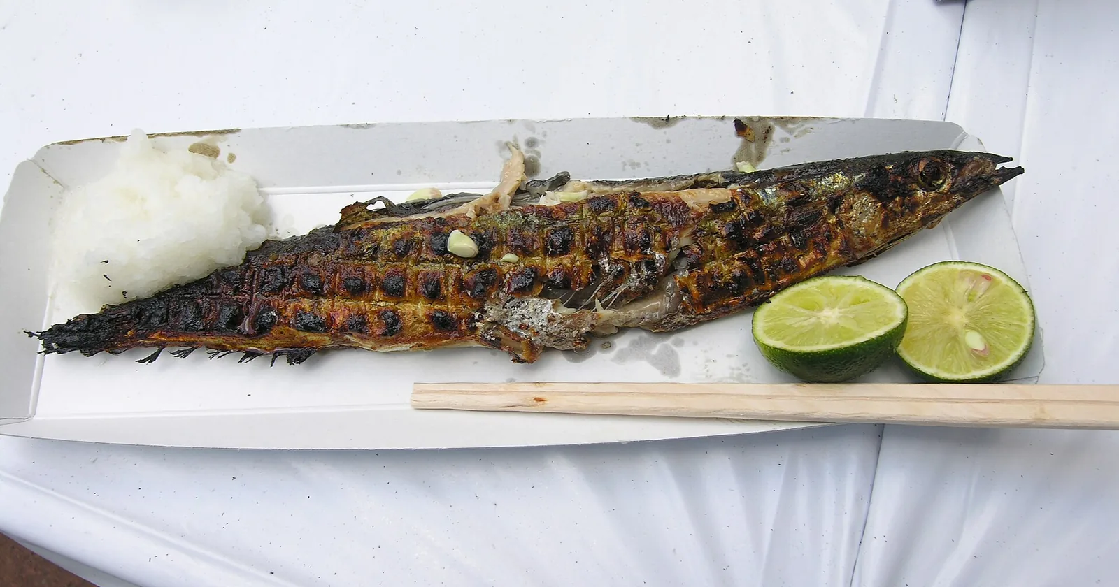 Grilled whole saury on a paper tray with grated daikon and lime