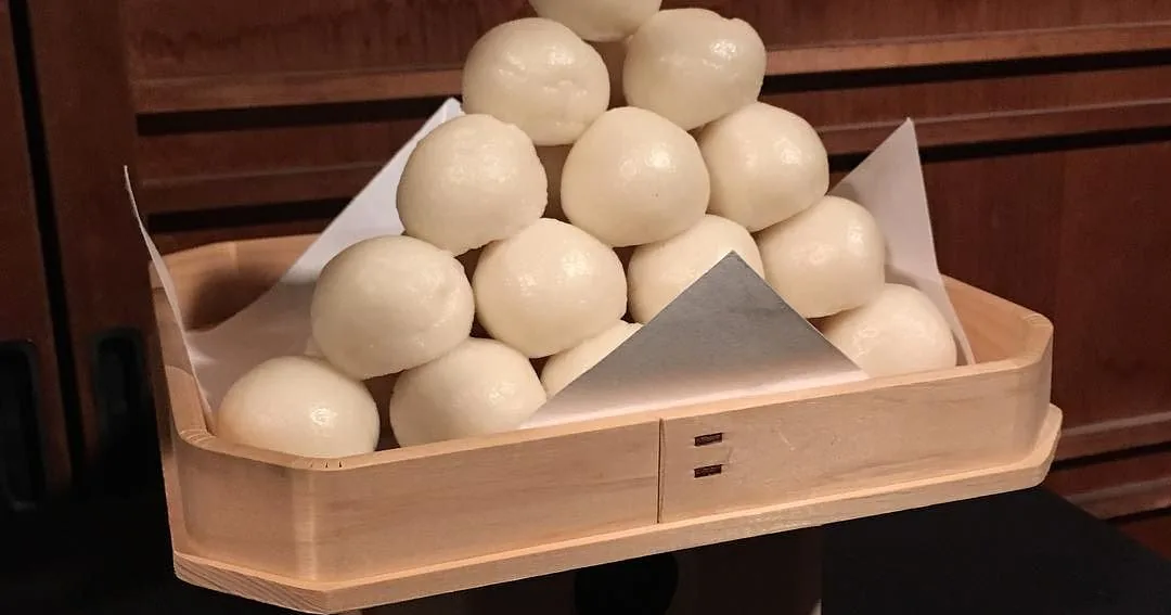A pyramid of white tsukimi dango stacked on a wooden sanbo offering tray.