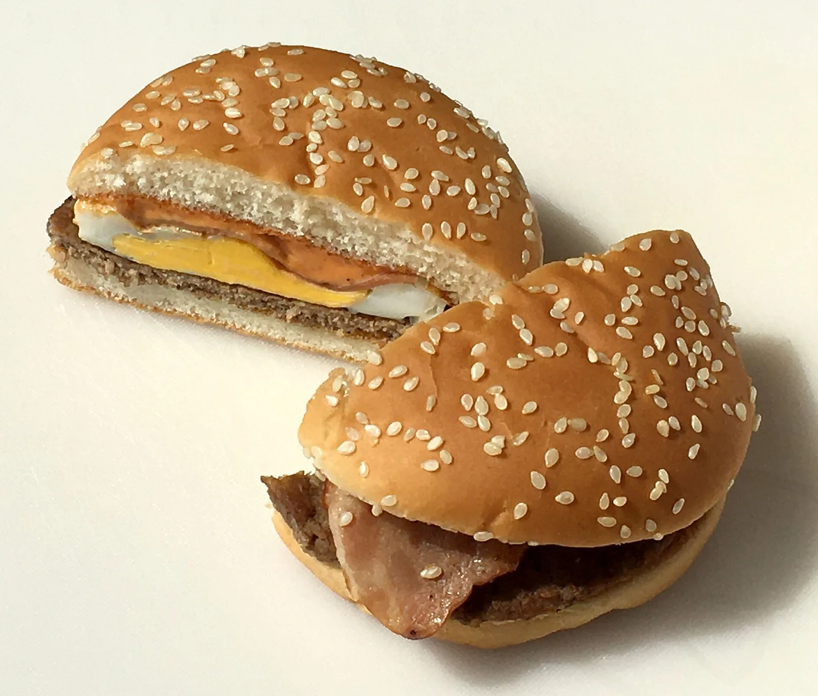 A McDonald's Japan Tsukimi Burger cut in half, showing the round egg, bacon, cheese and beef patty inside a sesame bun.