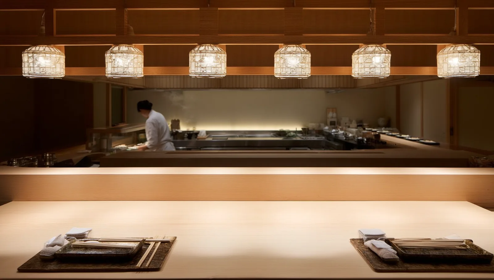 An intimate hinoki-wood sushi counter set with place settings for omakase guests under warm light.